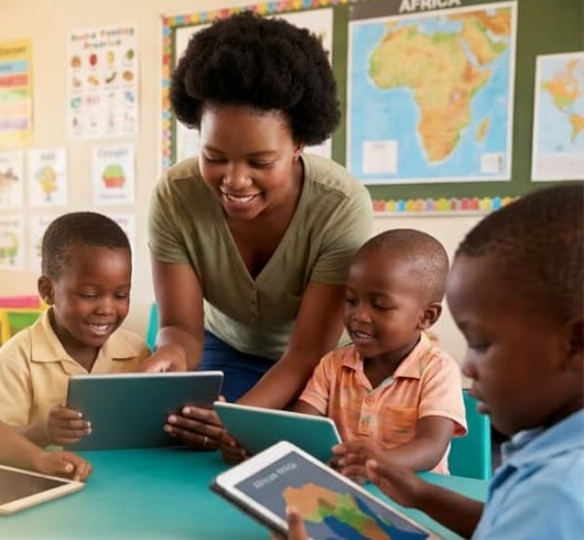A smiling teacher guides children working on tablets